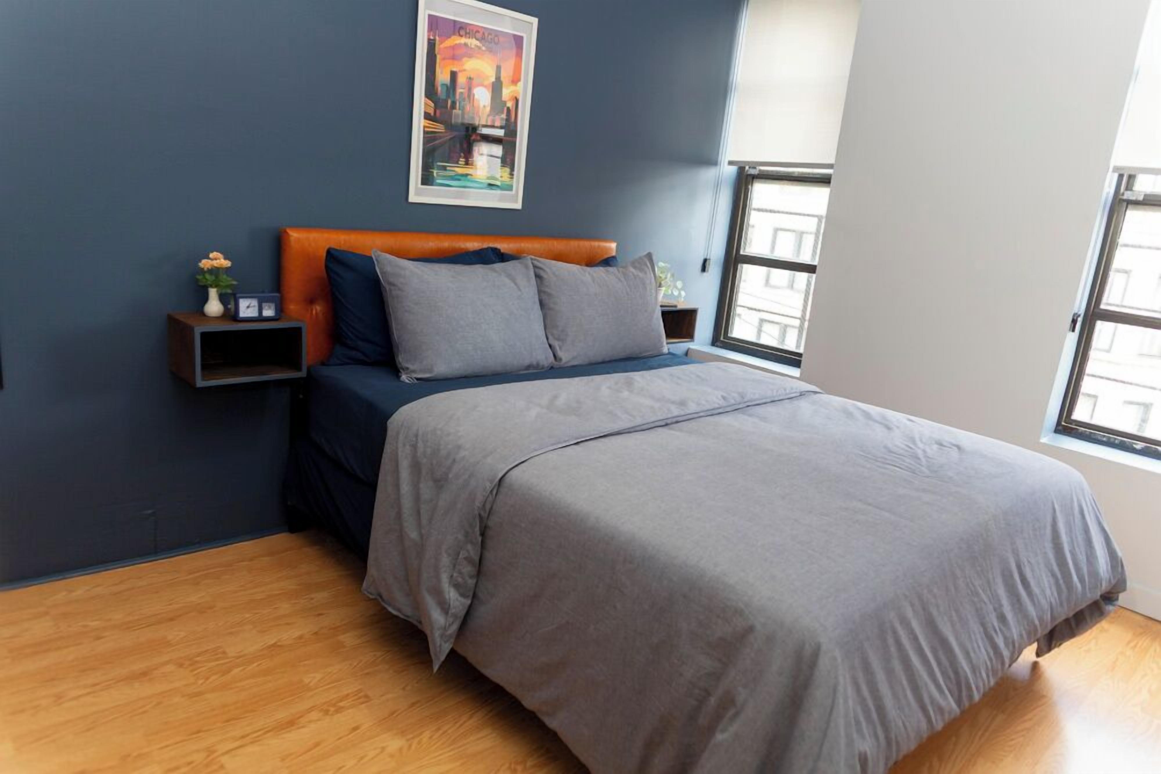 A bedroom with a bed, a nightstand, a wall clock, a framed picture, and a window.