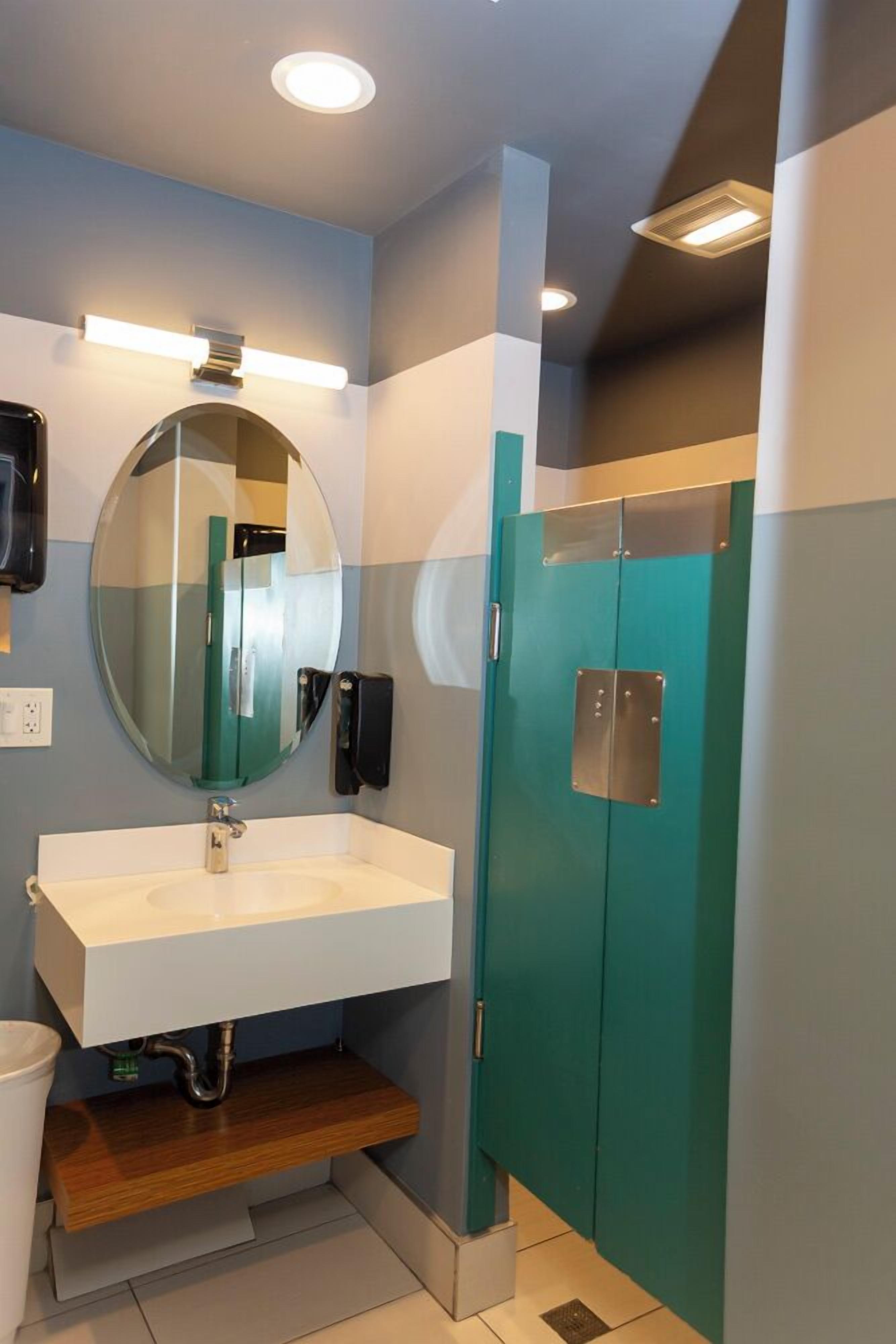 A modern bathroom with a white sink, a round mirror, a teal cabinet, and a light fixture above the mirror.