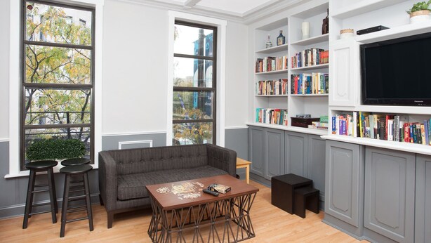 A modern living room with a grey sofa, a coffee table, and a bookshelf filled with books. - Chicago Parthenon Hostel (Chicago)