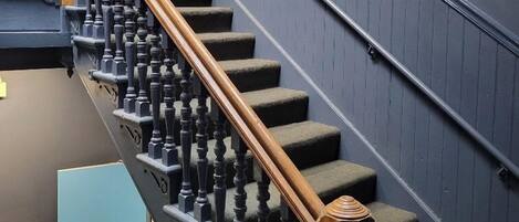 A staircase with a wooden handrail and black balusters, leading to a landing with a door marked "201 208".
