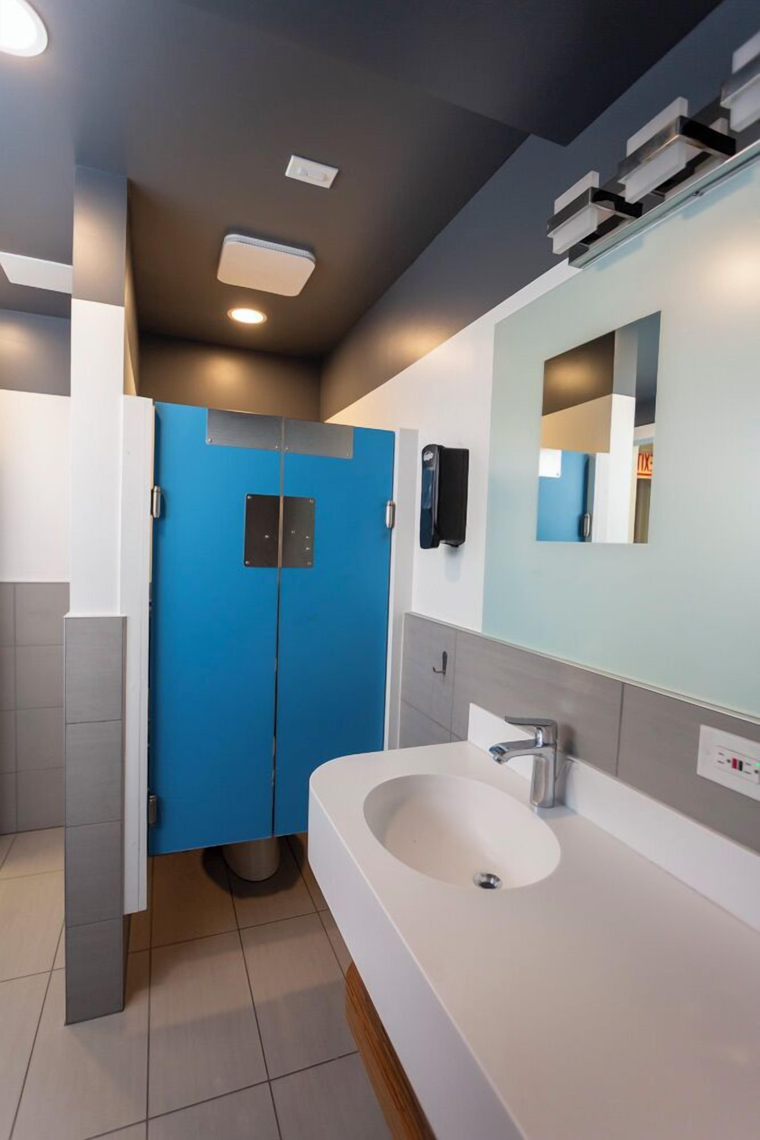 A modern bathroom with a large sink, a mirror, and a blue door.