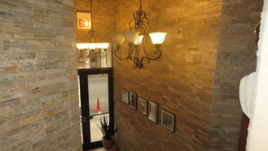 A hallway with a brick wall, a chandelier, and framed pictures. - Chicago Parthenon Hostel (Chicago)