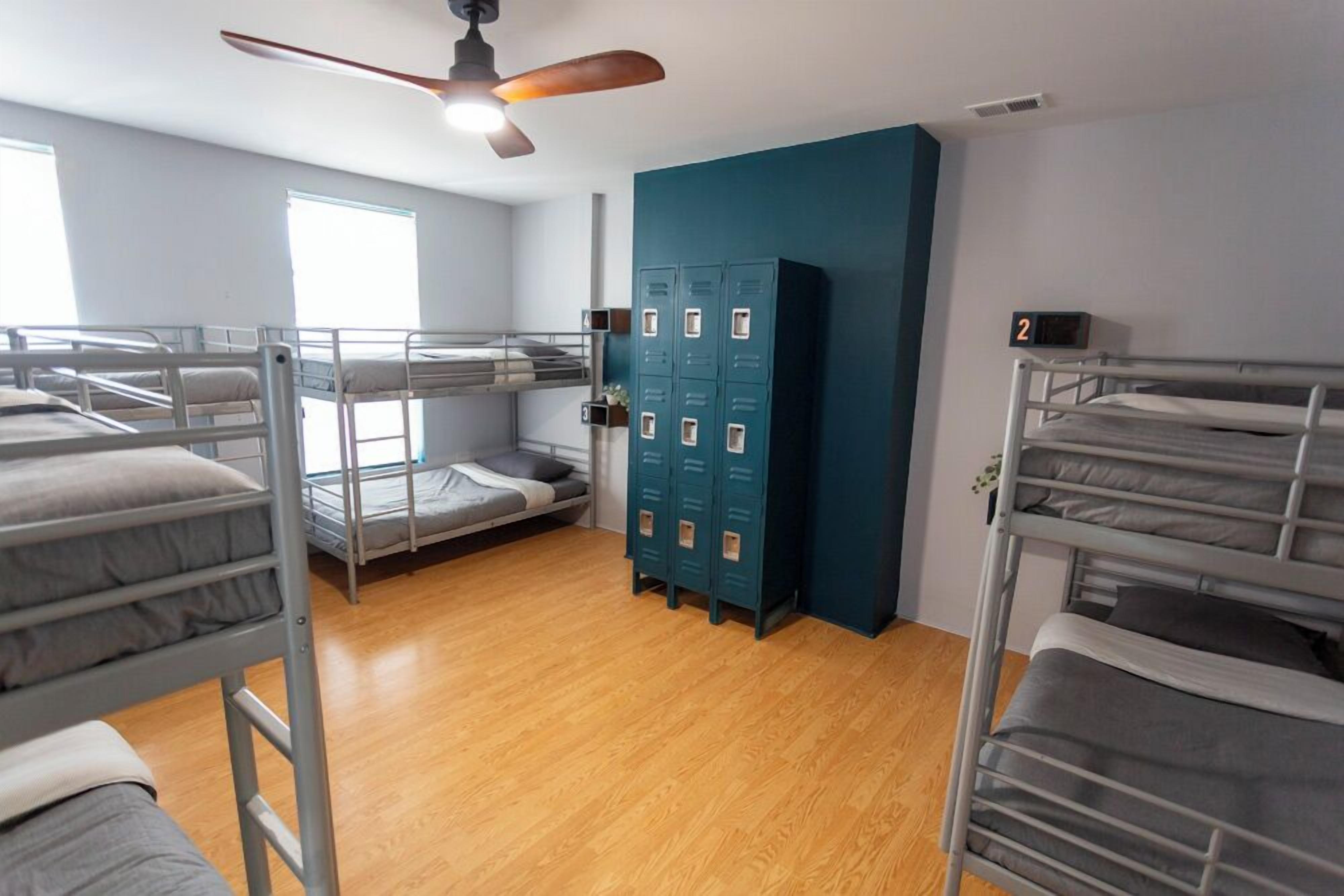 Une chambre de dortoir équipée de lits superposés, d’un ventilateur de plafond, d’une fenêtre et d’une rangée de casiers.