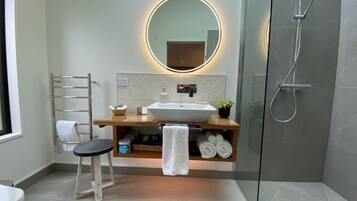 A modern bathroom with a glass-enclosed shower, a wooden vanity with a round mirror, and a towel rack.