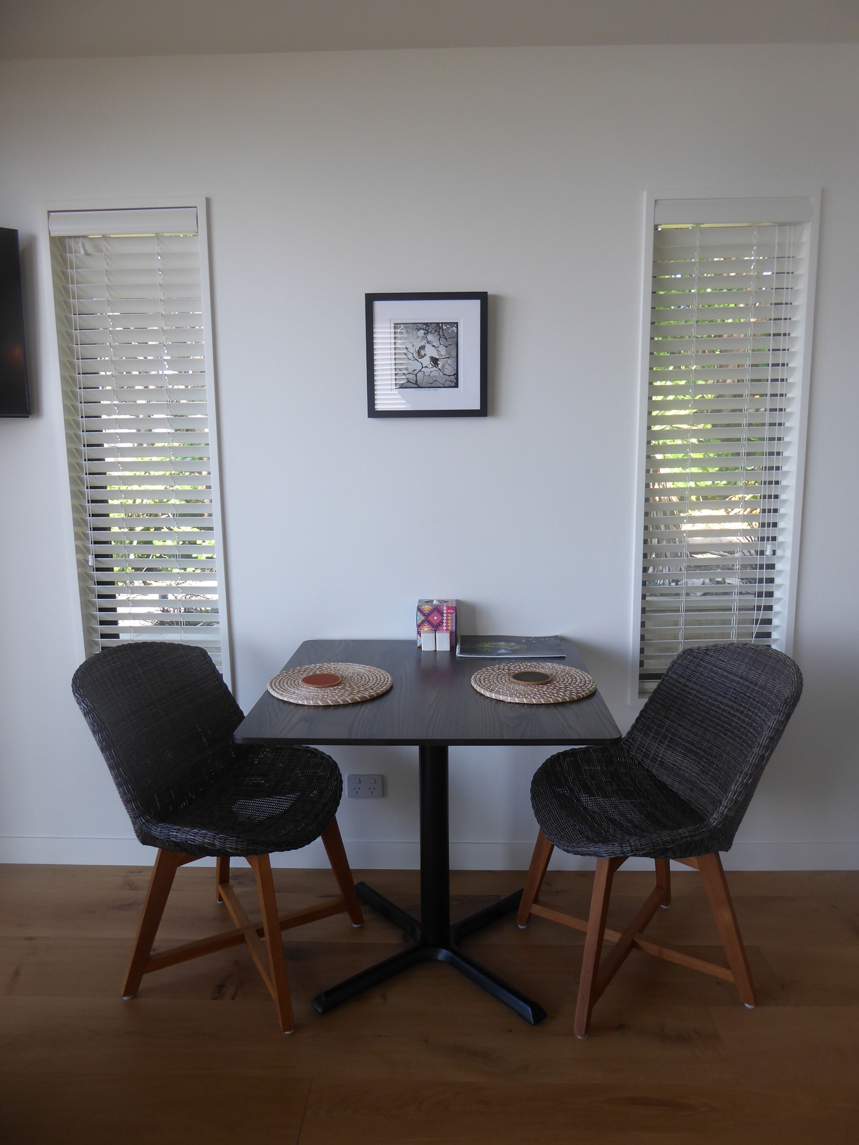 Un comedor con una mesa, dos sillas, un cuadro enmarcado y una ventana con persianas.