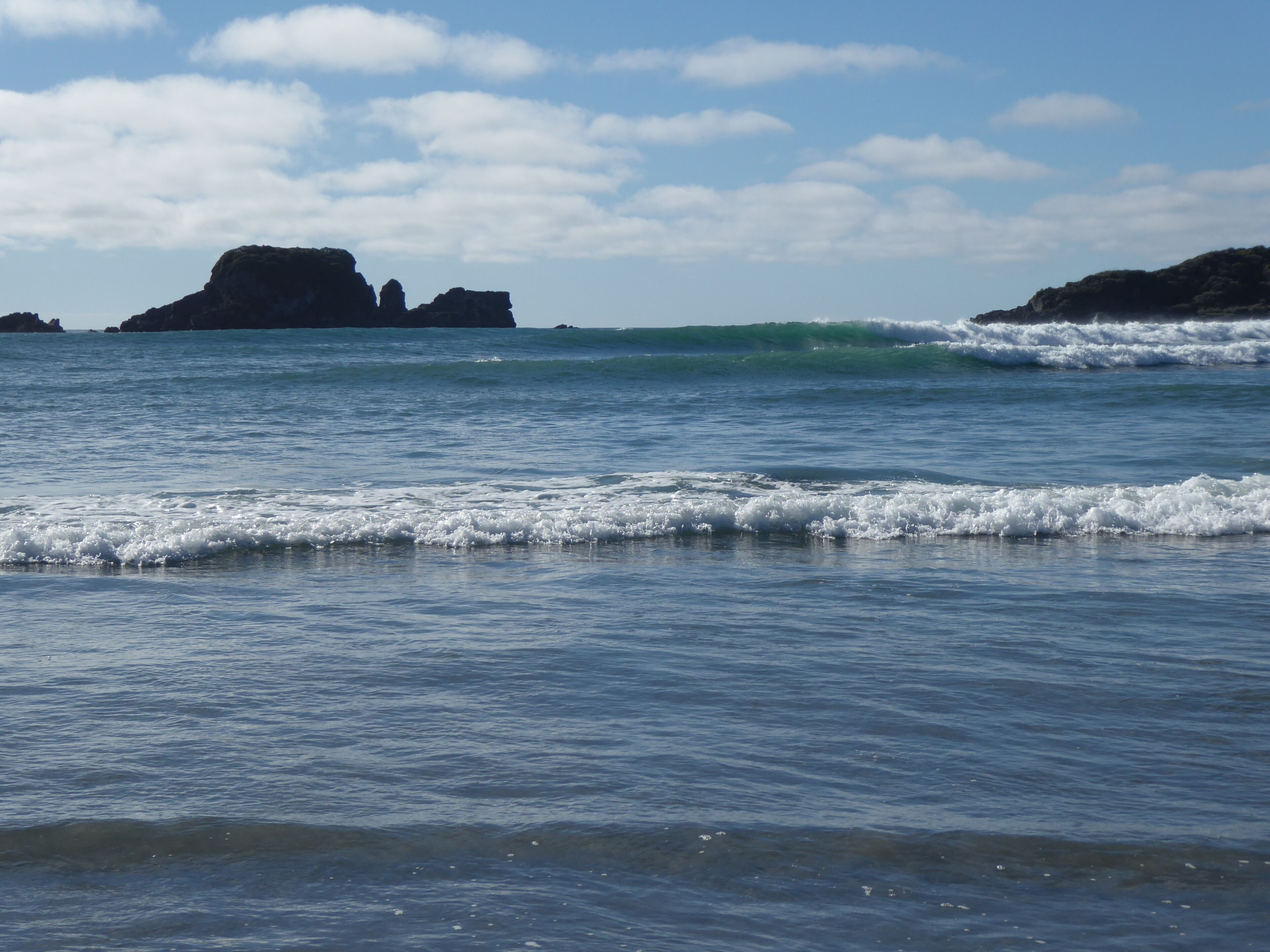 A coastal scene with calm waves and rocky outcrops under a clear sky.