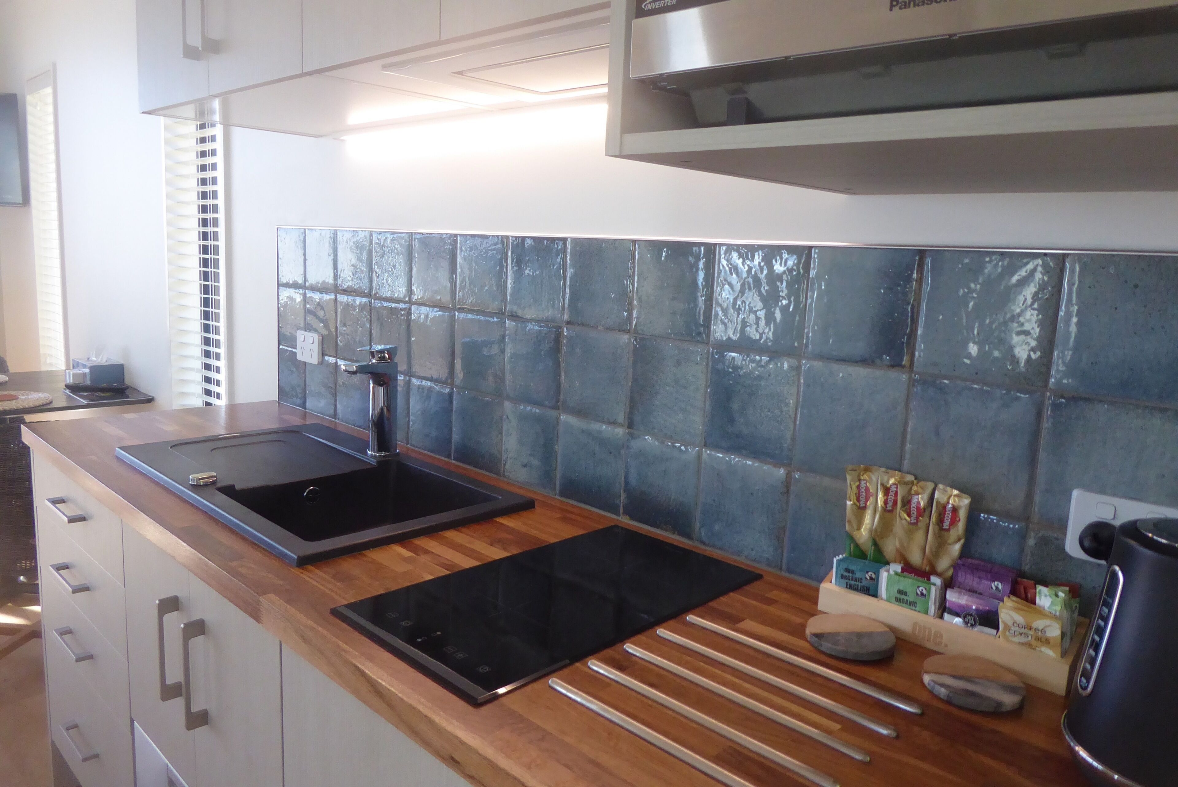 A modern kitchen with a black induction cooktop, a built-in oven, and a tiled backsplash.