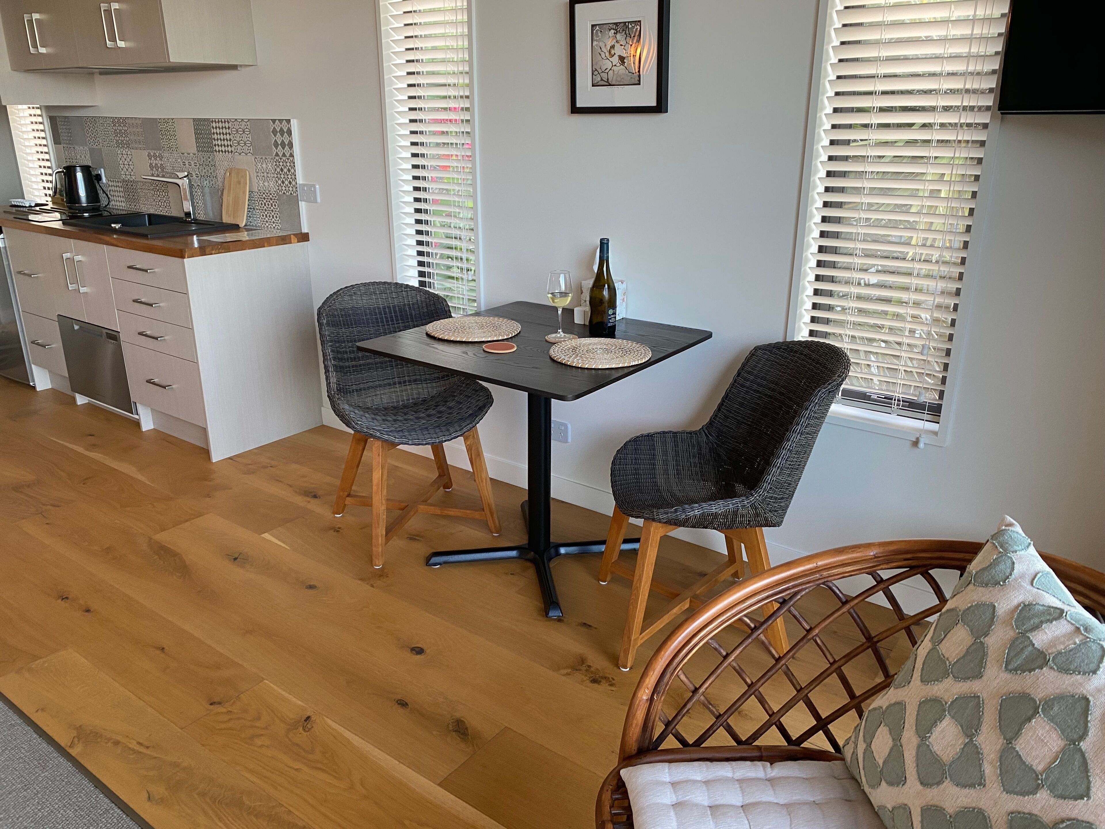 A modern kitchen with a dining area, featuring a table with chairs, a wine bottle, and a framed picture on the wall.