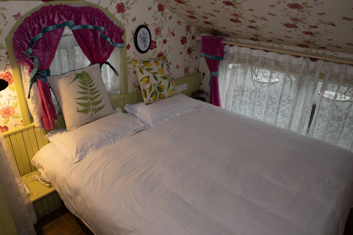 A bed with white linens, a wooden headboard, and floral wallpaper.