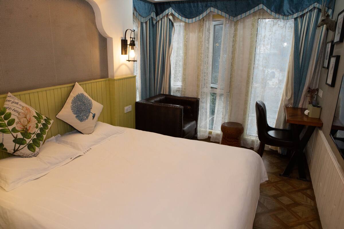 A bedroom with a bed, a chair, a small table, and a window with curtains.