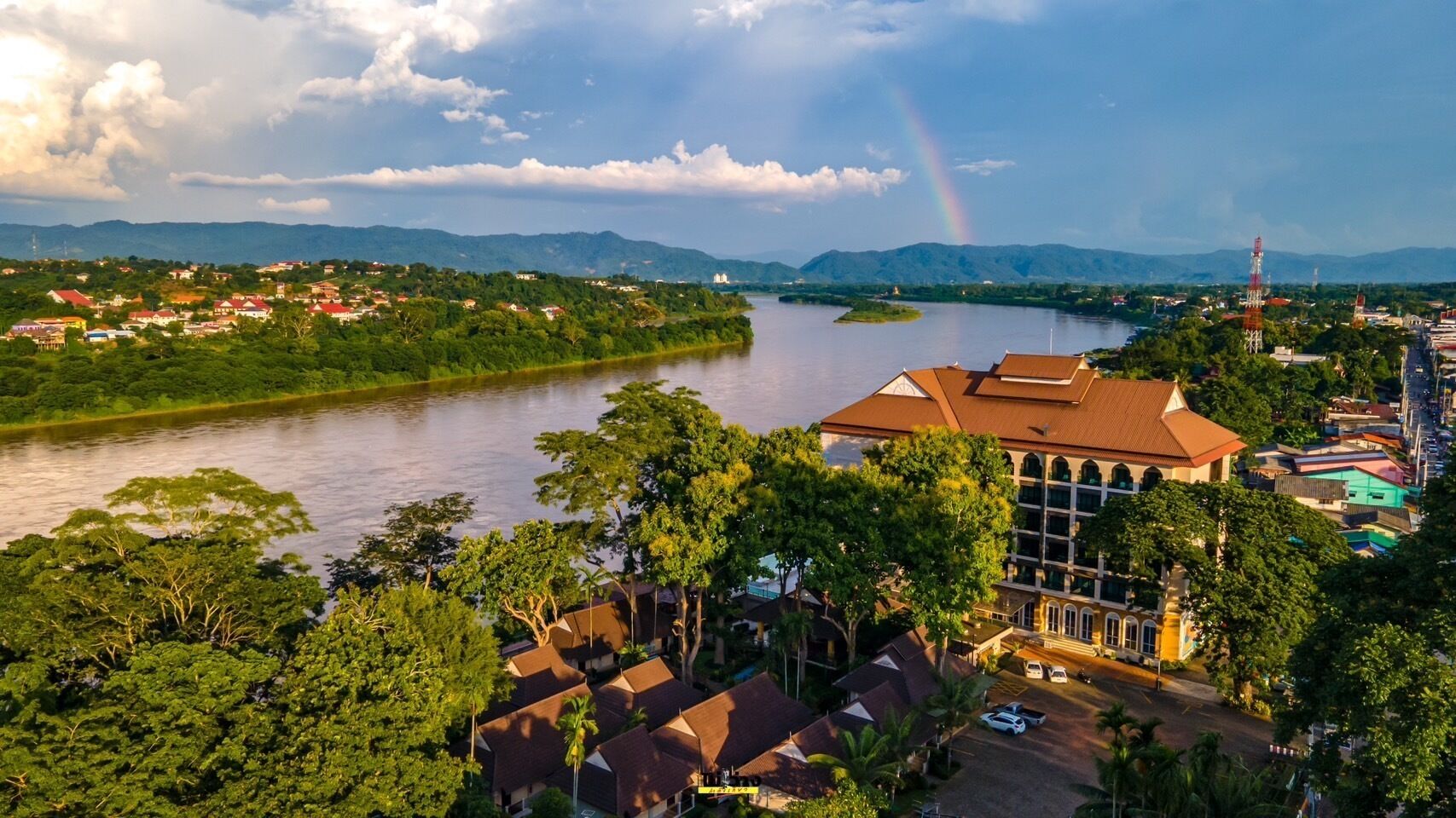 Une vue sur la rivière, avec un grand bâtiment, une végétation luxuriante et un arc-en-ciel lointain.
