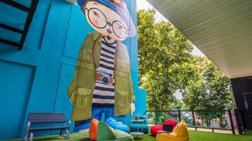 A colorful mural of a cartoon character on a building wall, outdoor seating with bean bags, and a green lawn area.