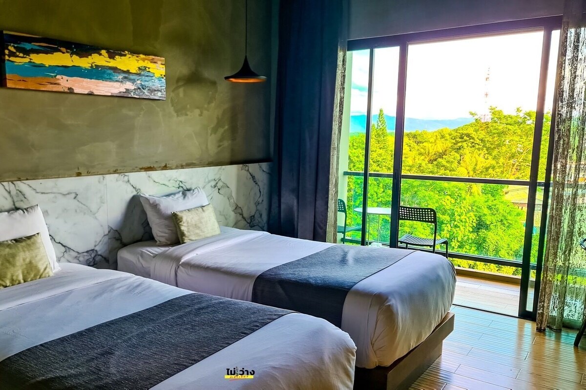 Ein Zimmer mit zwei Betten, einem Marmorkopfschild, einem Gemälde und einem großen Fenster mit Blick auf Grünflächen.