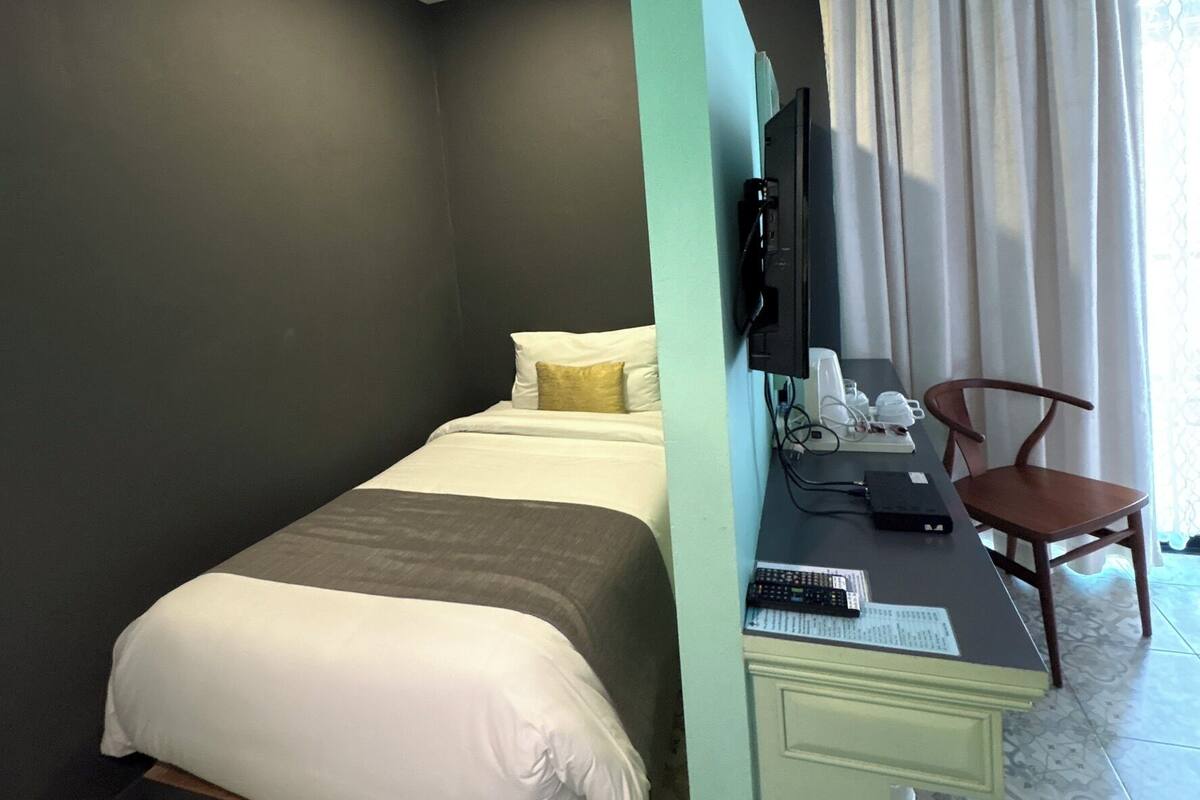 Habitación de hotel con cama, escritorio, silla, televisor y piso estampado.