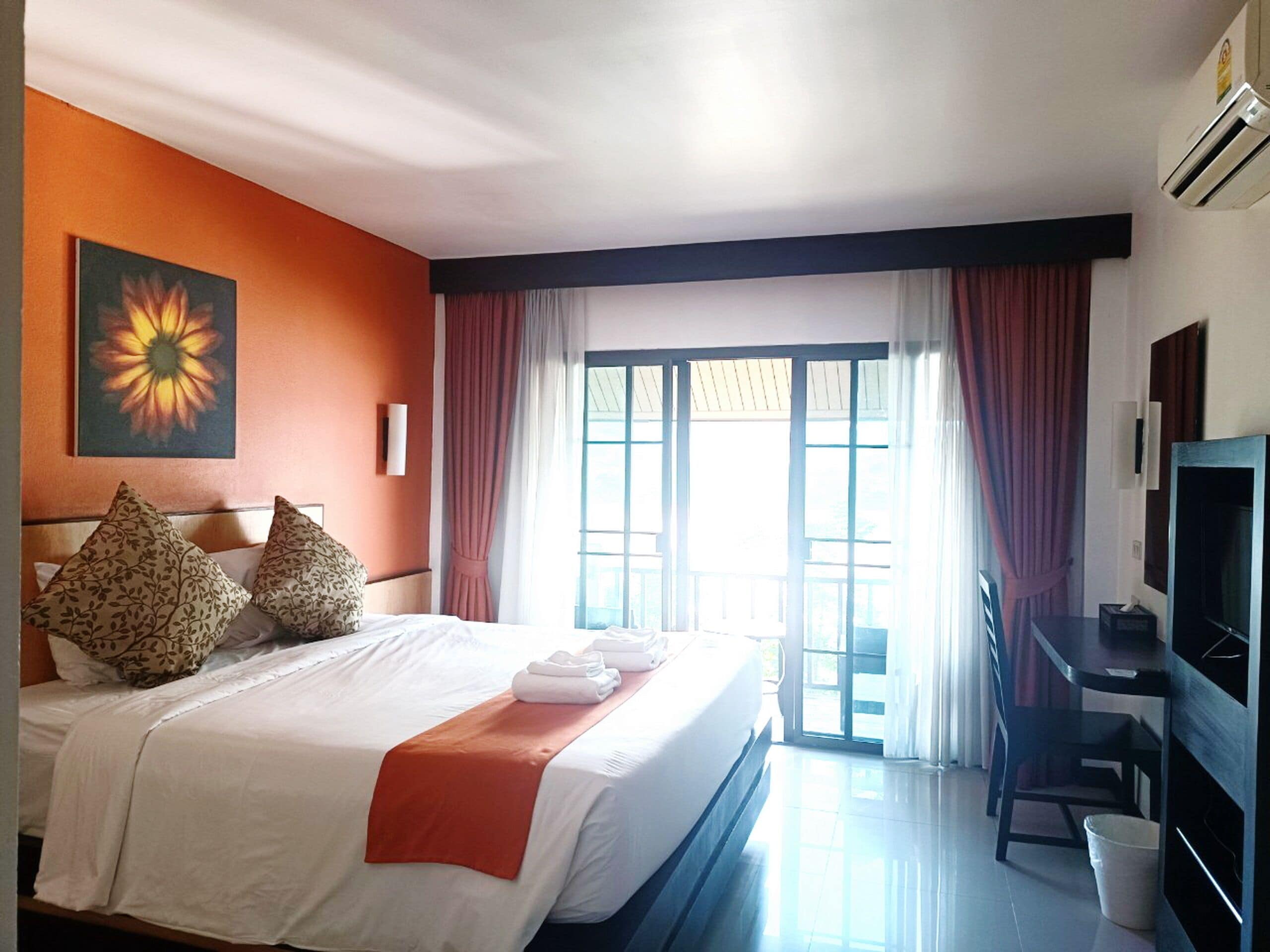 Une chambre d’hôtel avec un lit, un bureau, une télévision et une fenêtre avec des rideaux.
