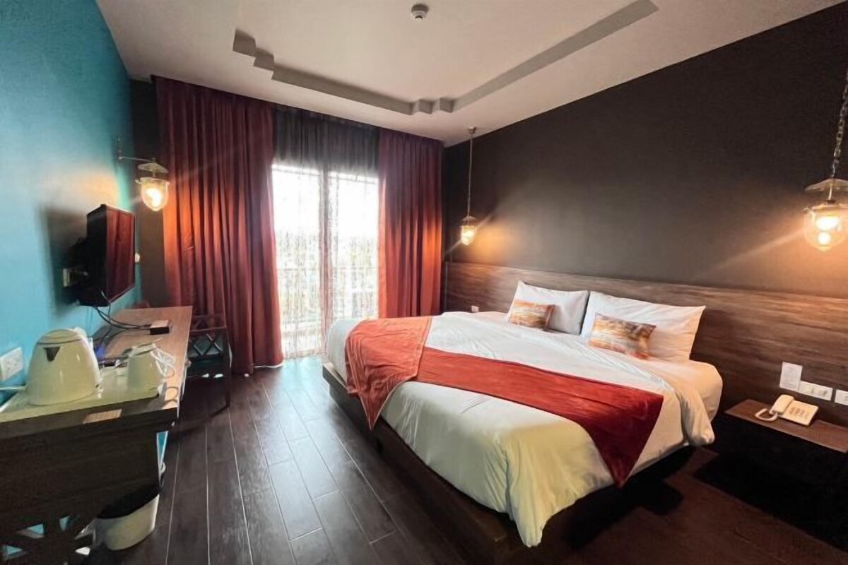 A hotel room with a large bed, a desk with a telephone, and a window with curtains.
