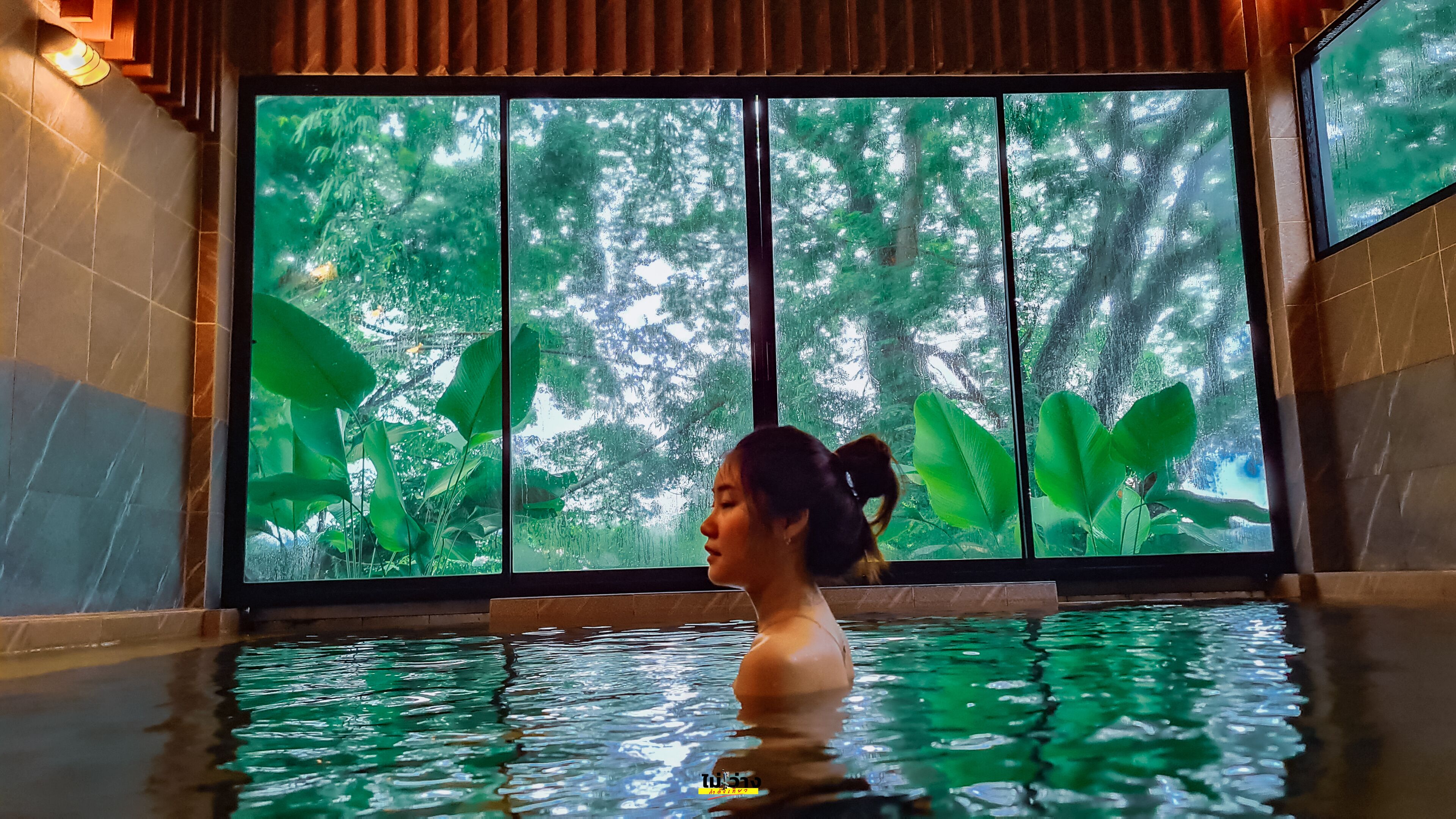 Una persona en una piscina con un ventanal que ofrece vistas a un bosque.