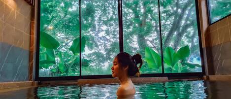 Una persona en una piscina con un ventanal que ofrece vistas a un bosque.