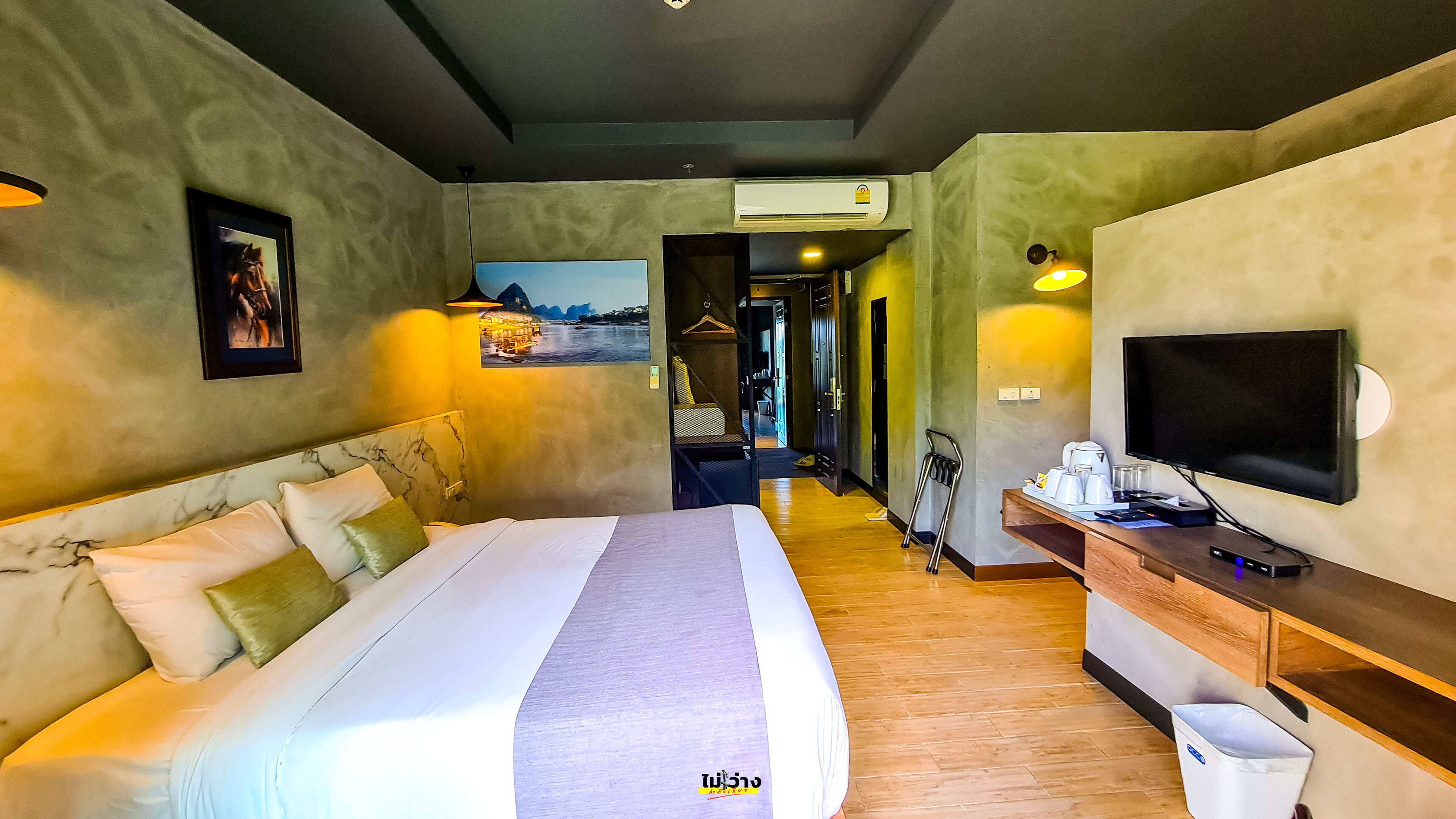 A hotel room with a large bed, a TV, a desk with a coffee maker, and a view of a water body through the window.