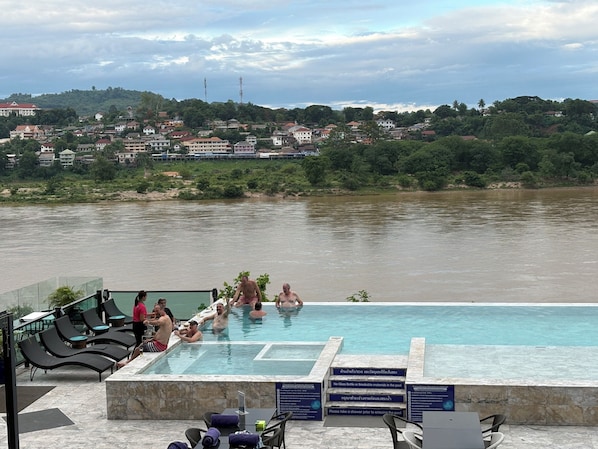 Ein Swimmingpool mit Liegestühlen und Blick auf einen Fluss sowie Häuser im Hintergrund.