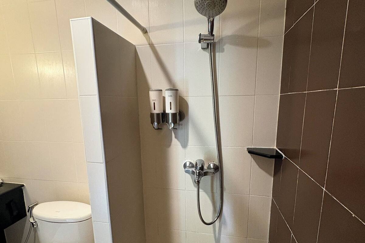 Un baño pequeño con ducha, inodoro y dos dispensadores de jabón de manos fijados a la pared.