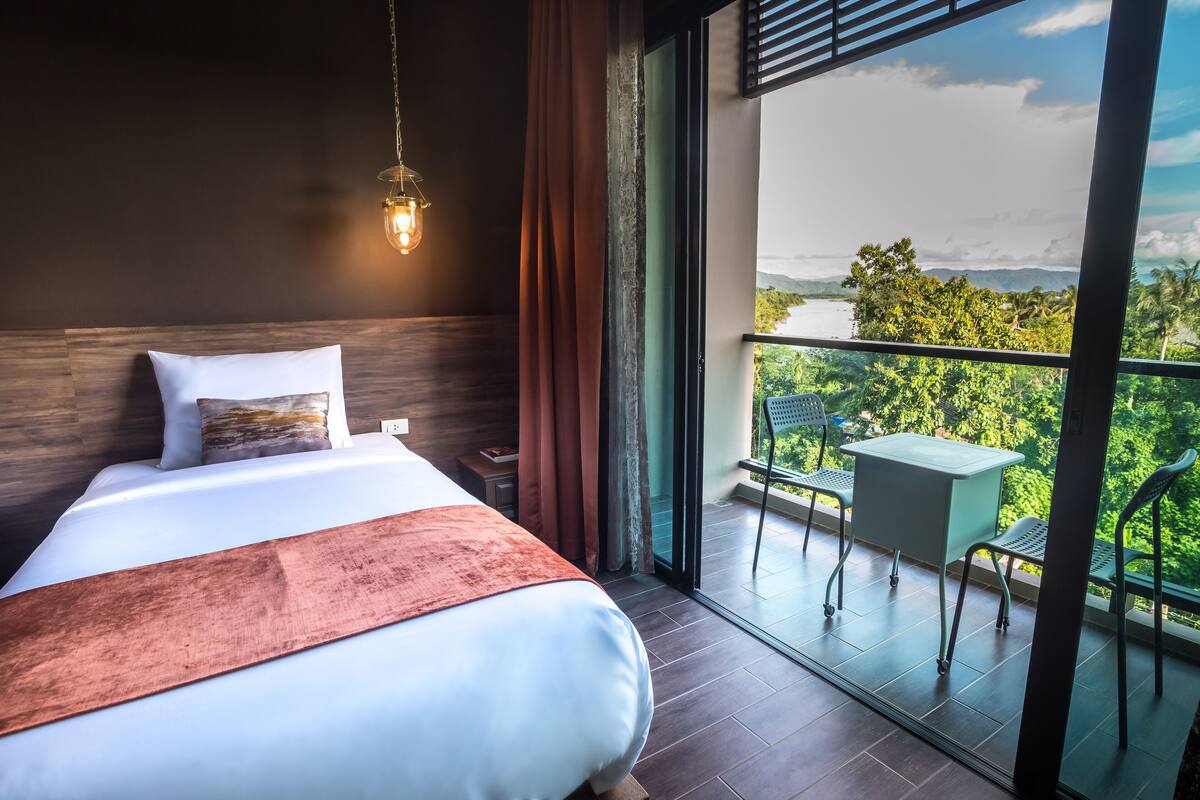 Habitación de hotel moderna con una cama grande, y vistas a exuberante vegetación y montañas desde un balcón.