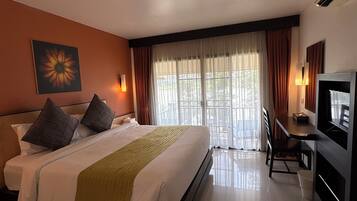 Una habitación de hotel con cama, escritorio, televisor y ventana con cortinas.