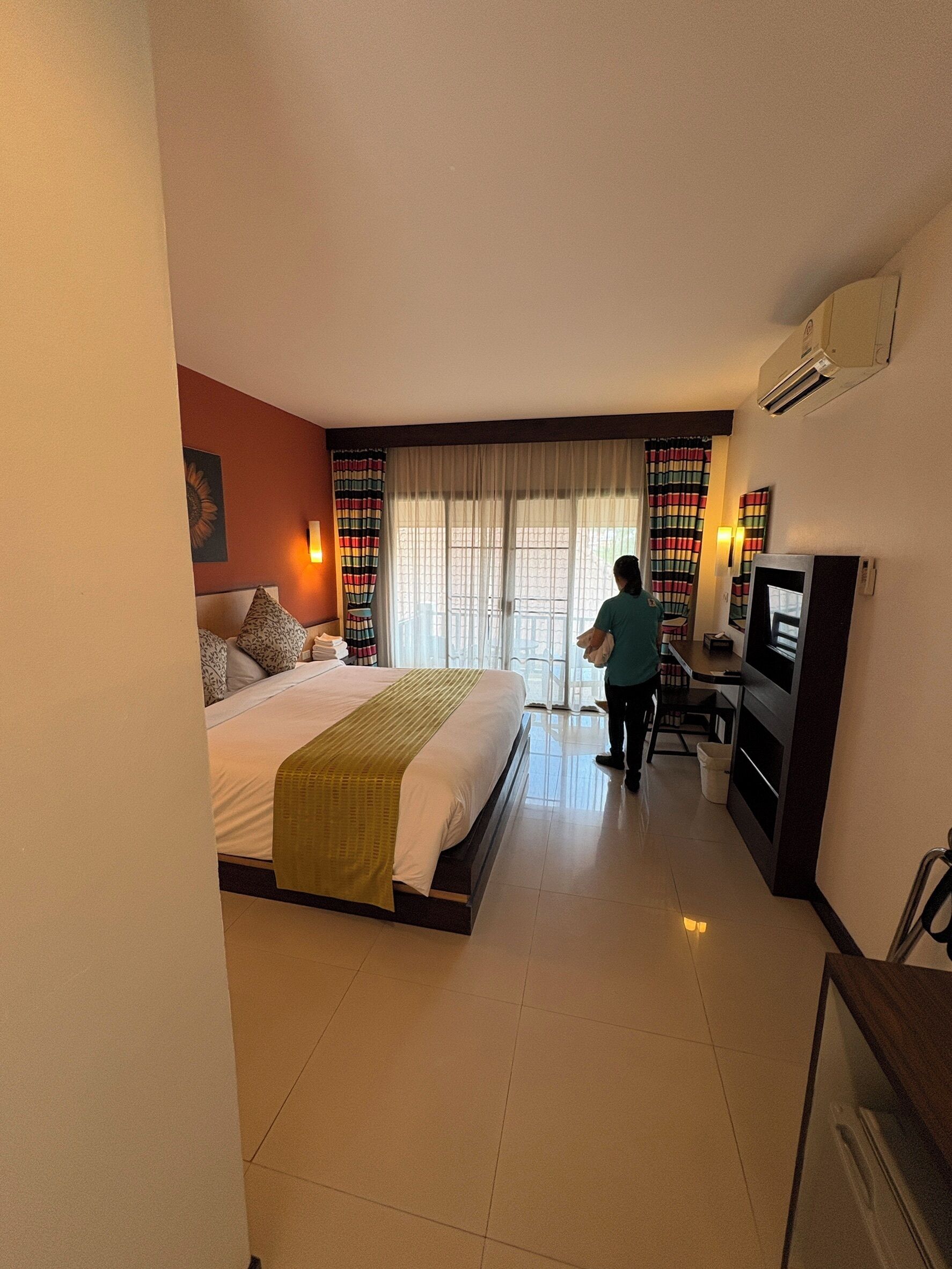 A hotel room with a bed, a desk, a television, and a window with curtains.