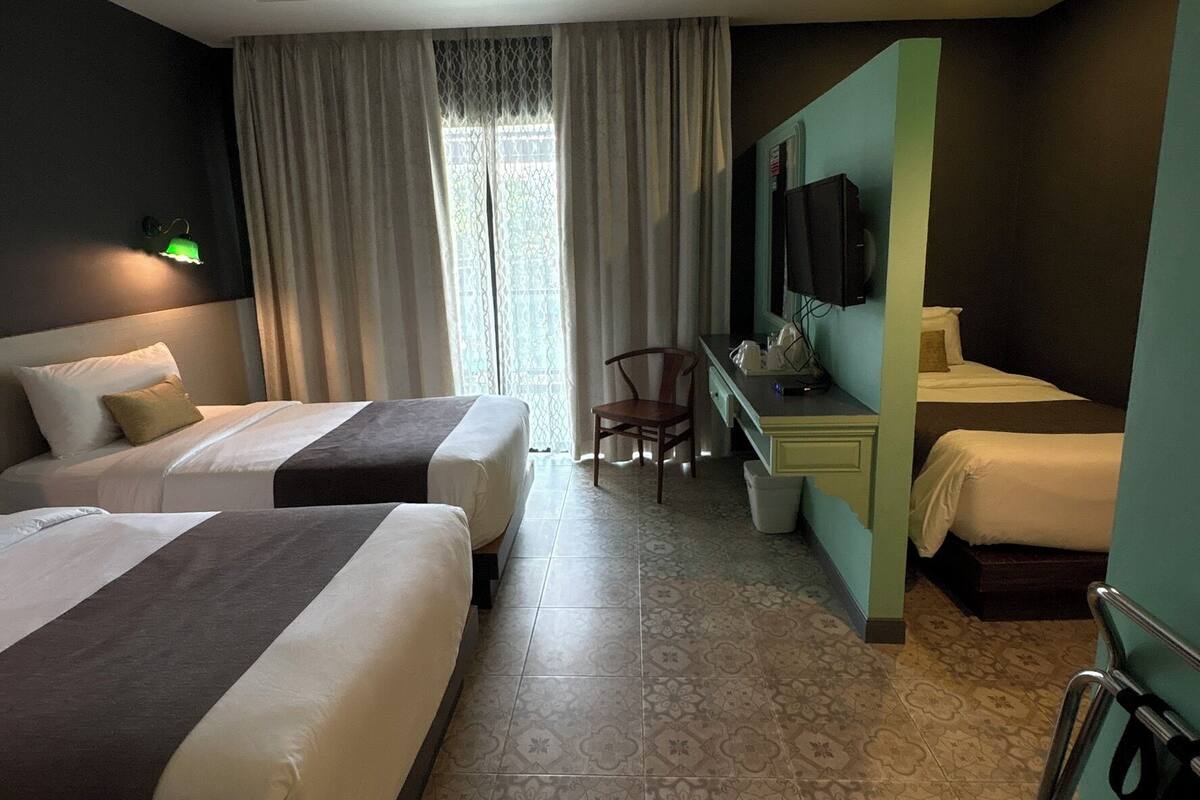Habitación de hotel con dos camas, un escritorio, una silla, un televisor y una ventana con cortinas.