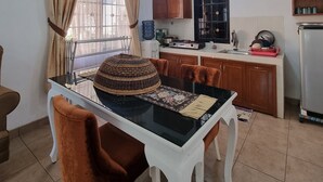 A dining area with a glass-top table, brown cushioned chairs, and a woven basket on the table. - Kota Bunga A (Cipanas)