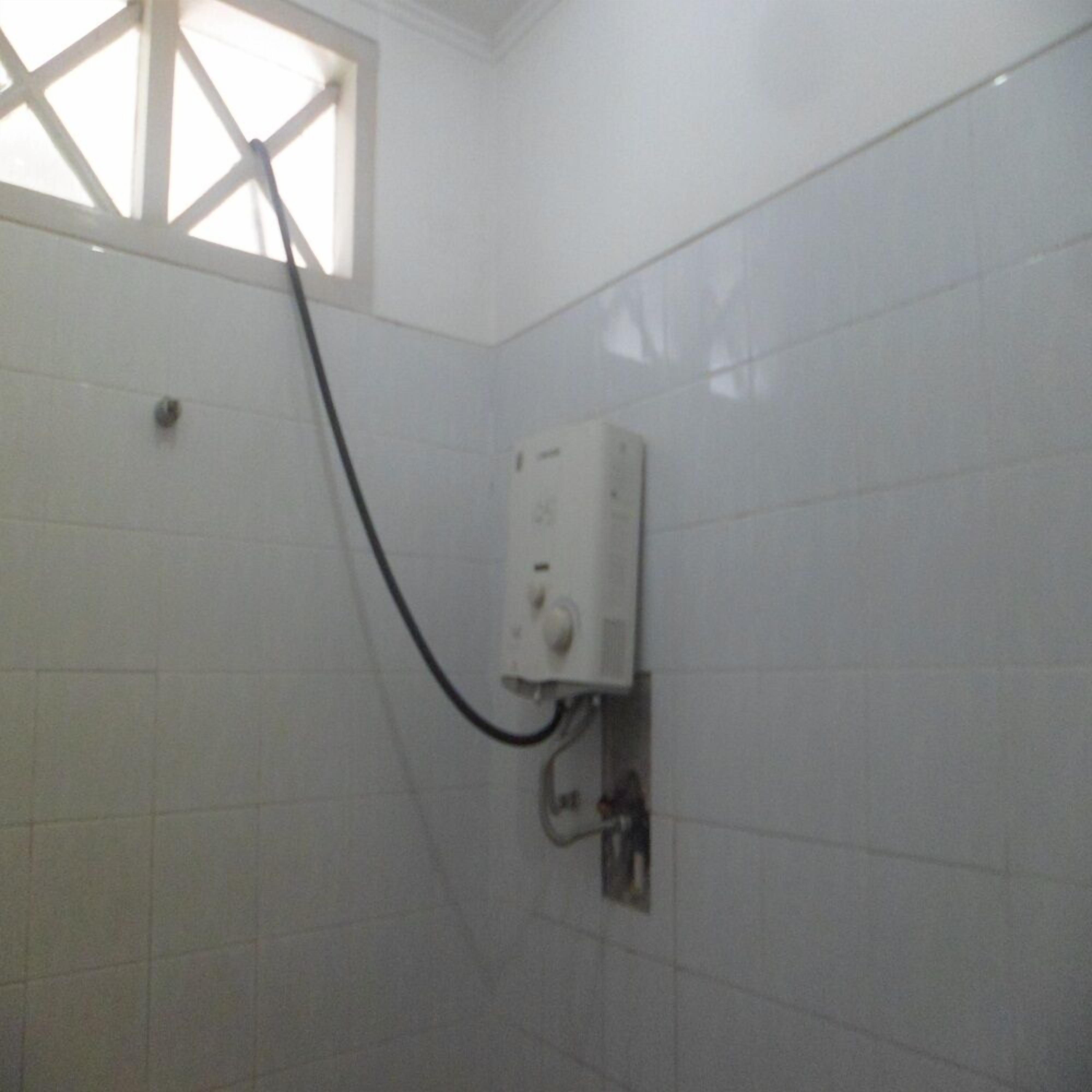 Un baño con paredes de azulejos blancos, una ventana con diseño de entramado y un calentador de pared con panel de control.
