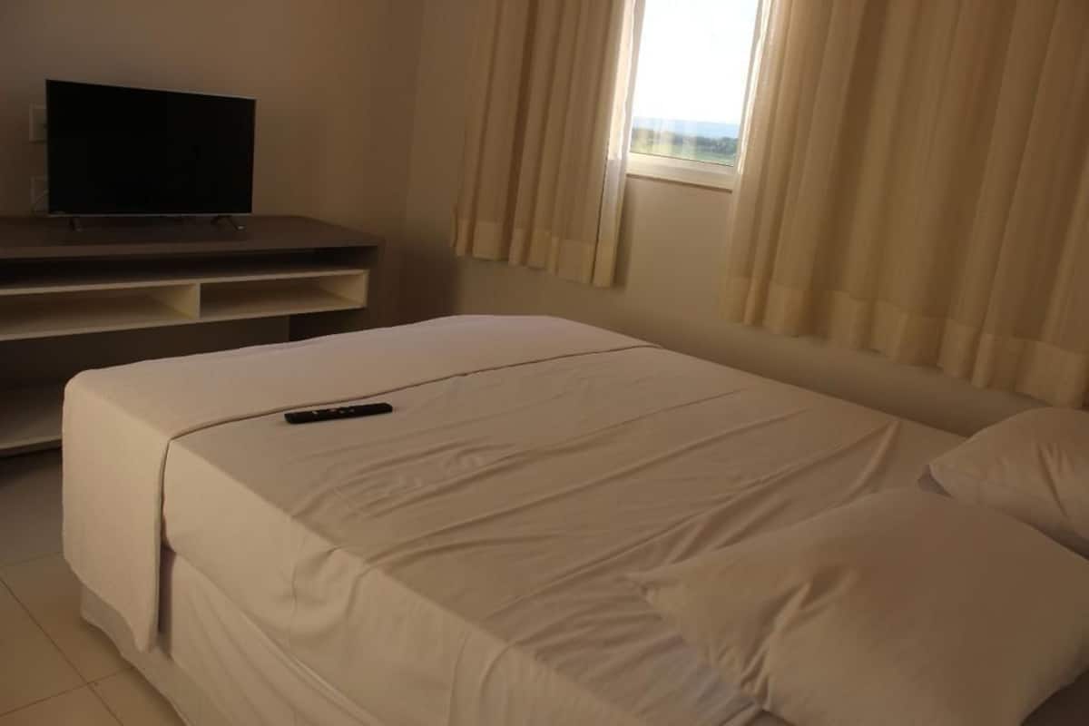 A hotel room with a bed, a TV on a stand, and a window with curtains.