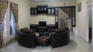 A living room with a sofa set, a television, and a staircase leading to another level. - Kota Bunga C (Cipanas)