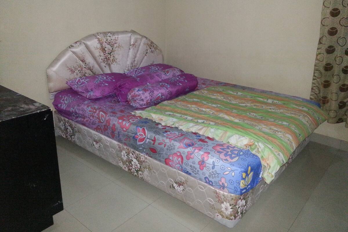 Una cama con colcha y almohadas estampadas con motivos florales, un cabecero y una cortina.