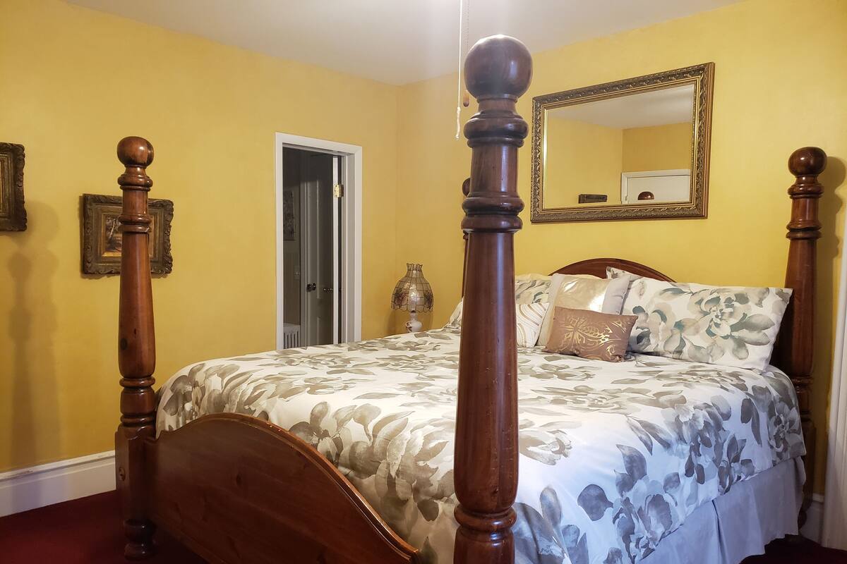 Un lit à baldaquin avec une literie à motifs floraux, un miroir au-dessus et une porte donnant sur une autre pièce.