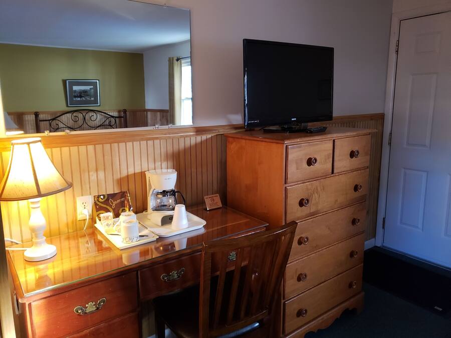 Una camera d'albergo con una scrivania in legno, una macchina del caffè, un televisore sopra un comò e una lampada.