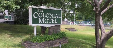 A sign for The Colonial Motel, surrounded by greenery and trees.