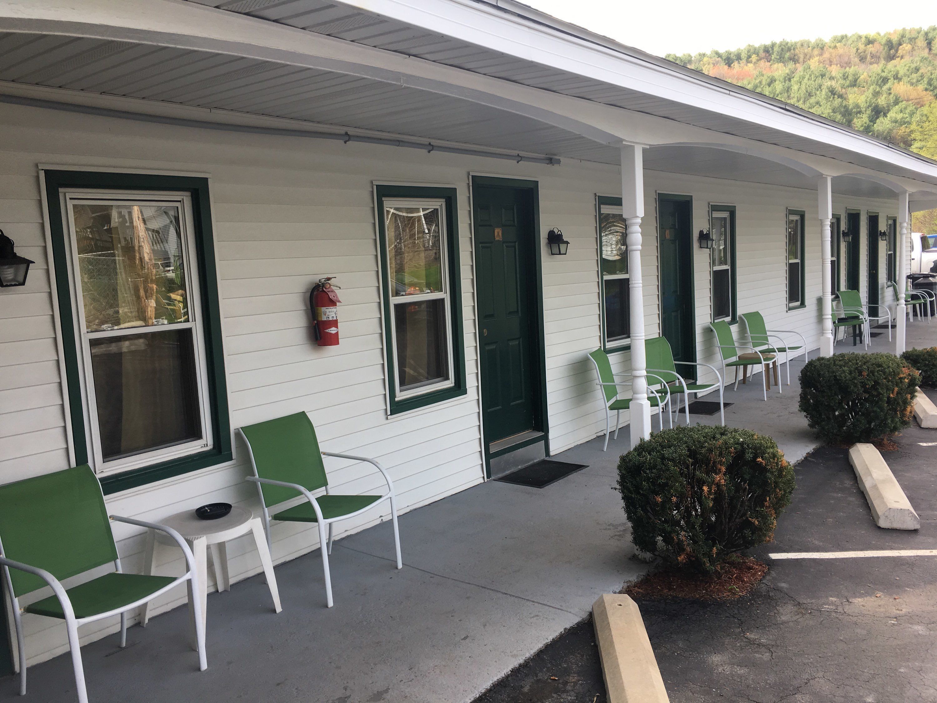 A motel with a covered porch, green-framed windows, and white chairs.