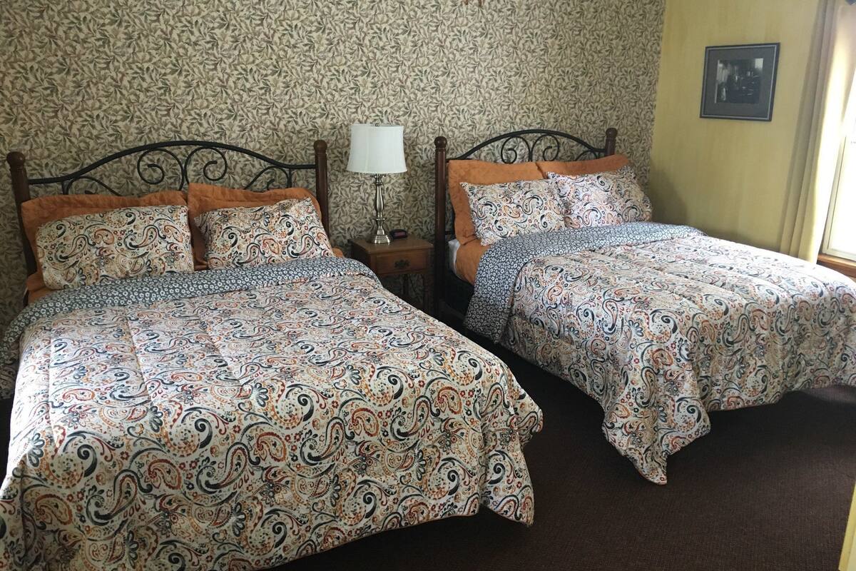 Une chambre avec deux lits, chacun agrémenté de draps à motifs, d’une lampe de chevet et d’un tableau encadré au mur.