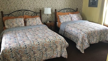 A room with two beds, each with patterned bedding, a bedside lamp, and a framed picture on the wall.