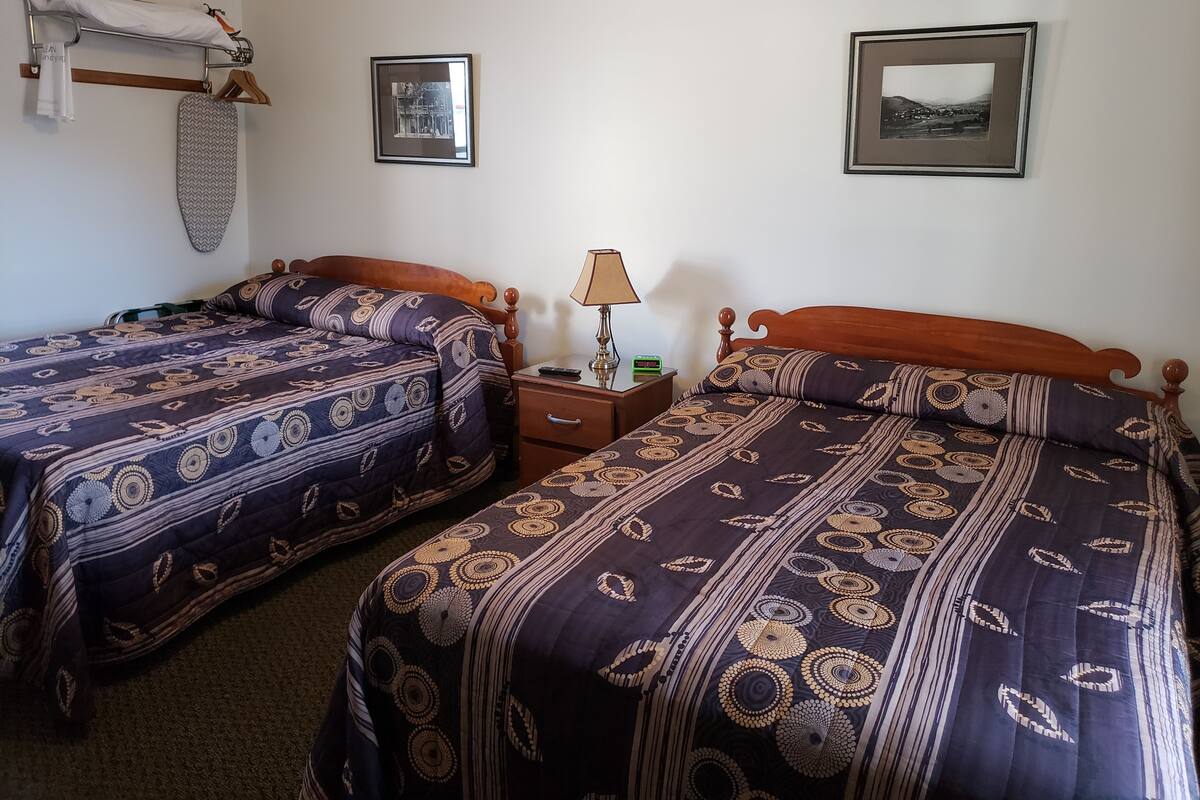 Une chambre avec deux lits, chacun agrémenté de draps à motifs, une table de chevet avec une lampe et un tableau encadré au mur.