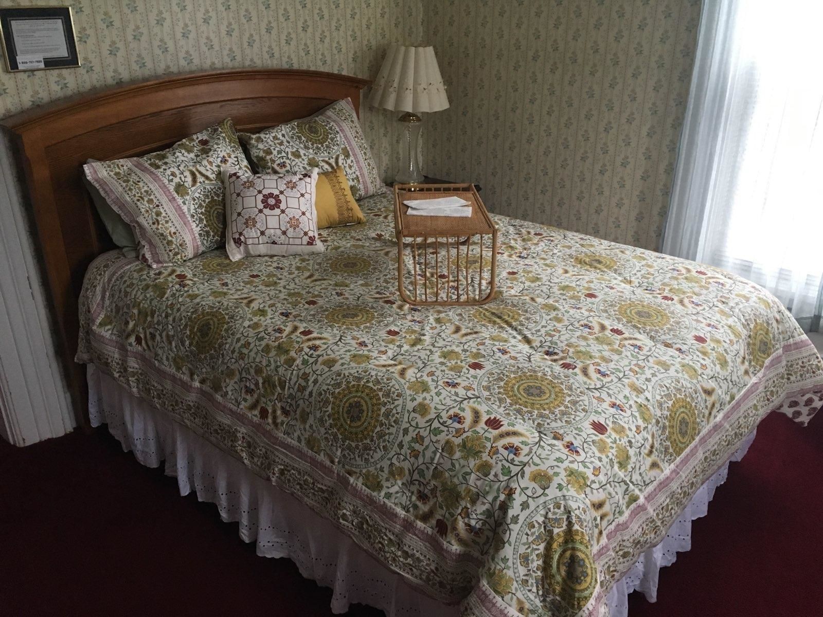 Un lit bien fait, recouvert d’une couvre-lit à motifs floraux, avec une tête de lit en bois et une table de chevet surmontée d’une lampe.
