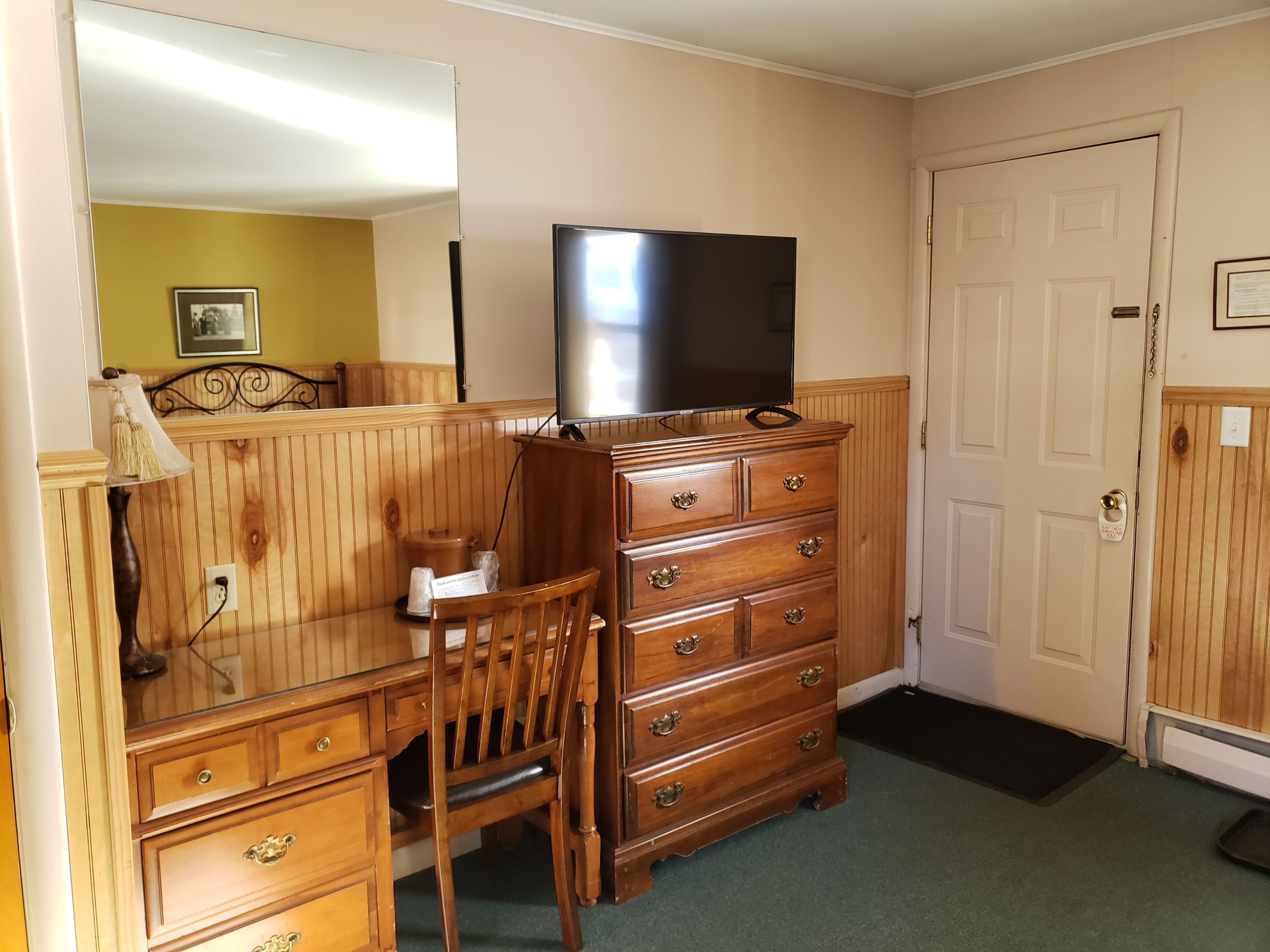 A room with a wooden dresser, a desk, a chair, a television, and a door.