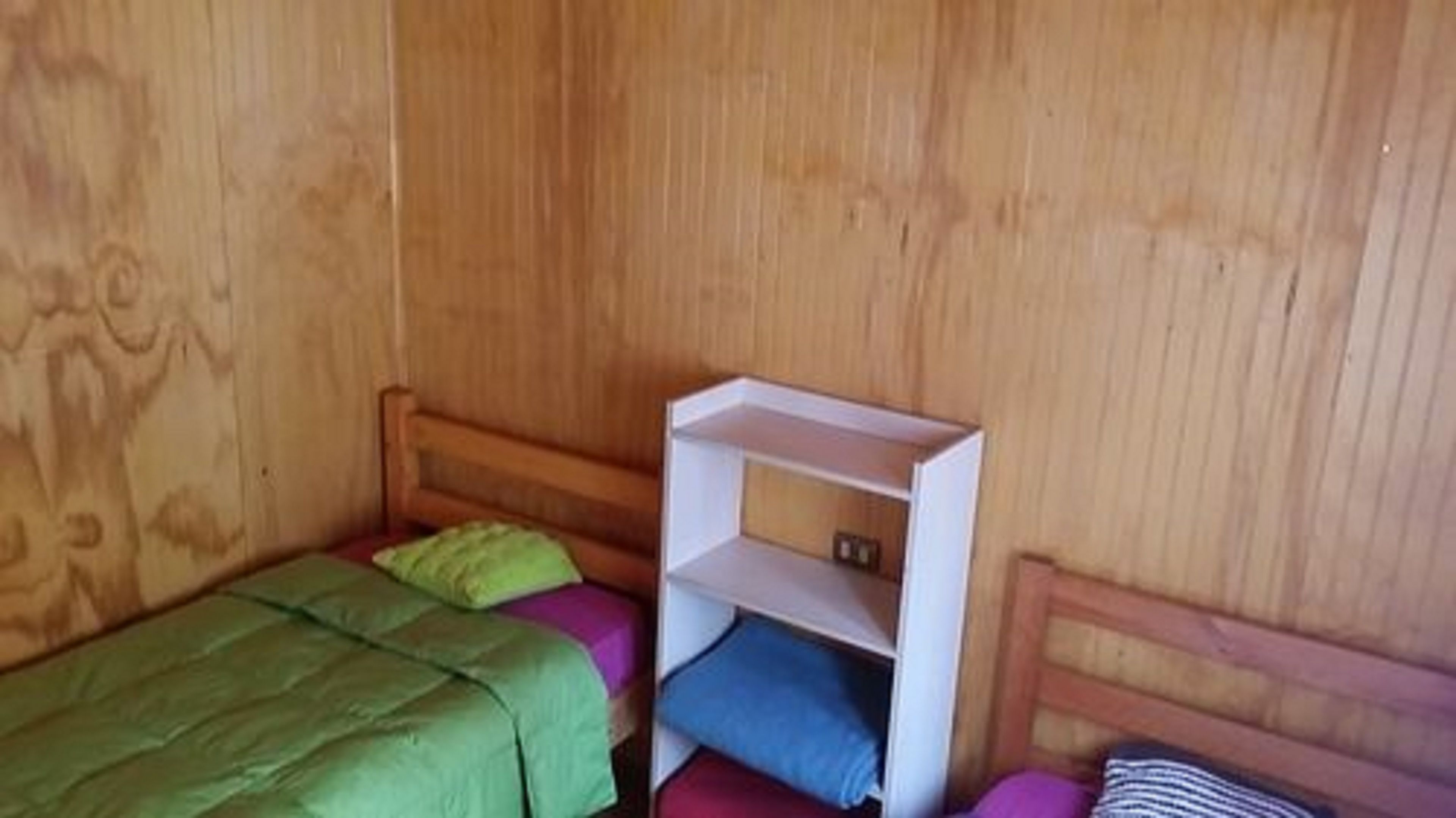 Um quarto pequeno de madeira com uma cama, uma mesa de cabeceira e uma estante.