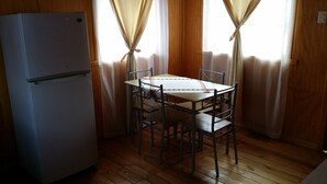 Una cocina compacta con un refrigerador blanco, una pequeña mesa de comedor con cuatro sillas y pisos de madera.