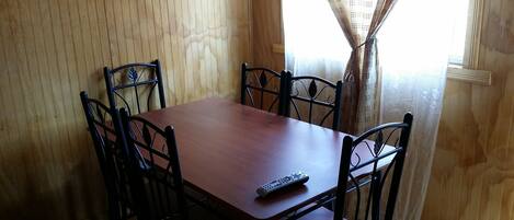 A dining table with four chairs, a remote control on the table, and a window with curtains.