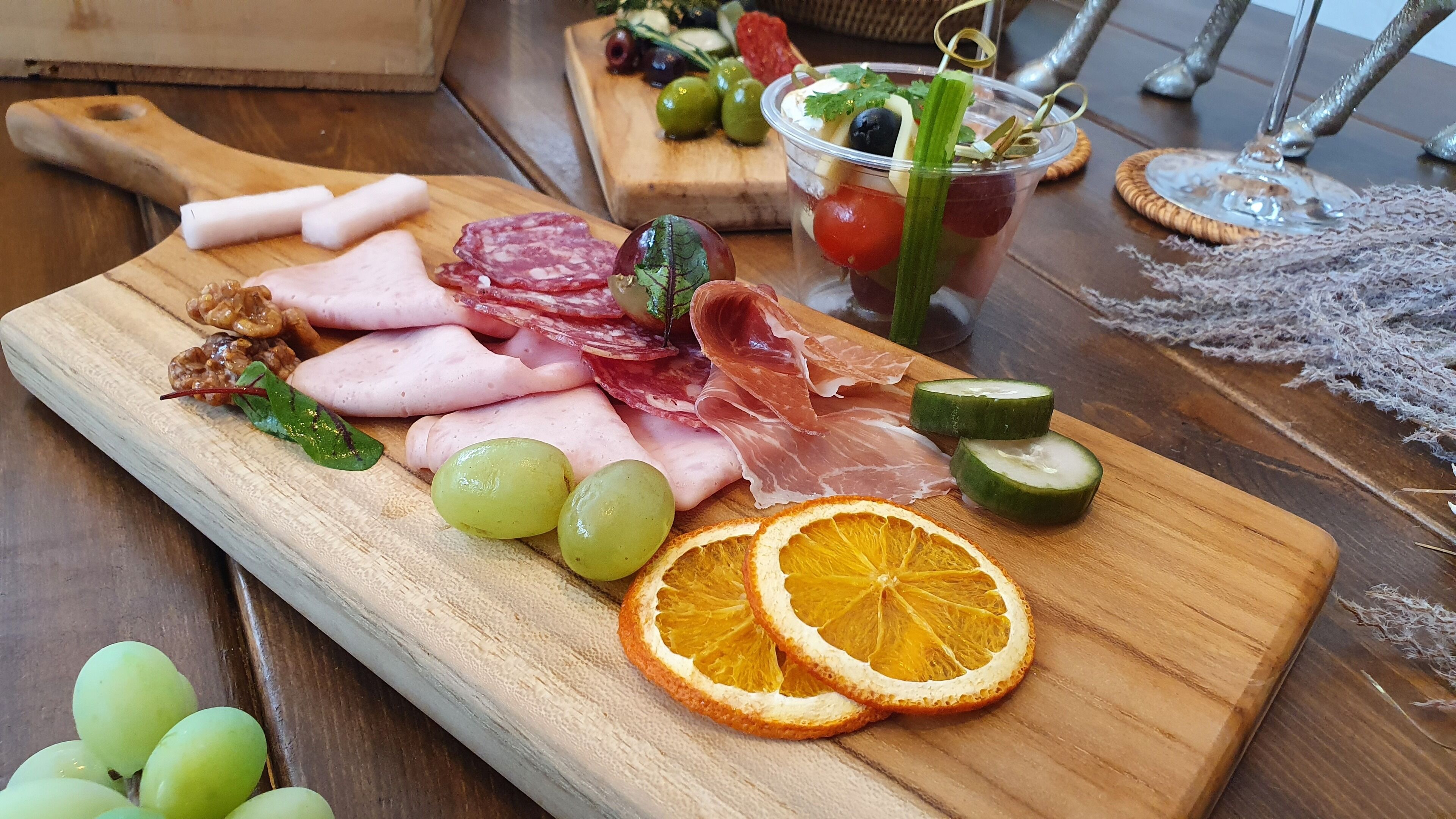 A wooden board with various meats, grapes, and dried orange slices.