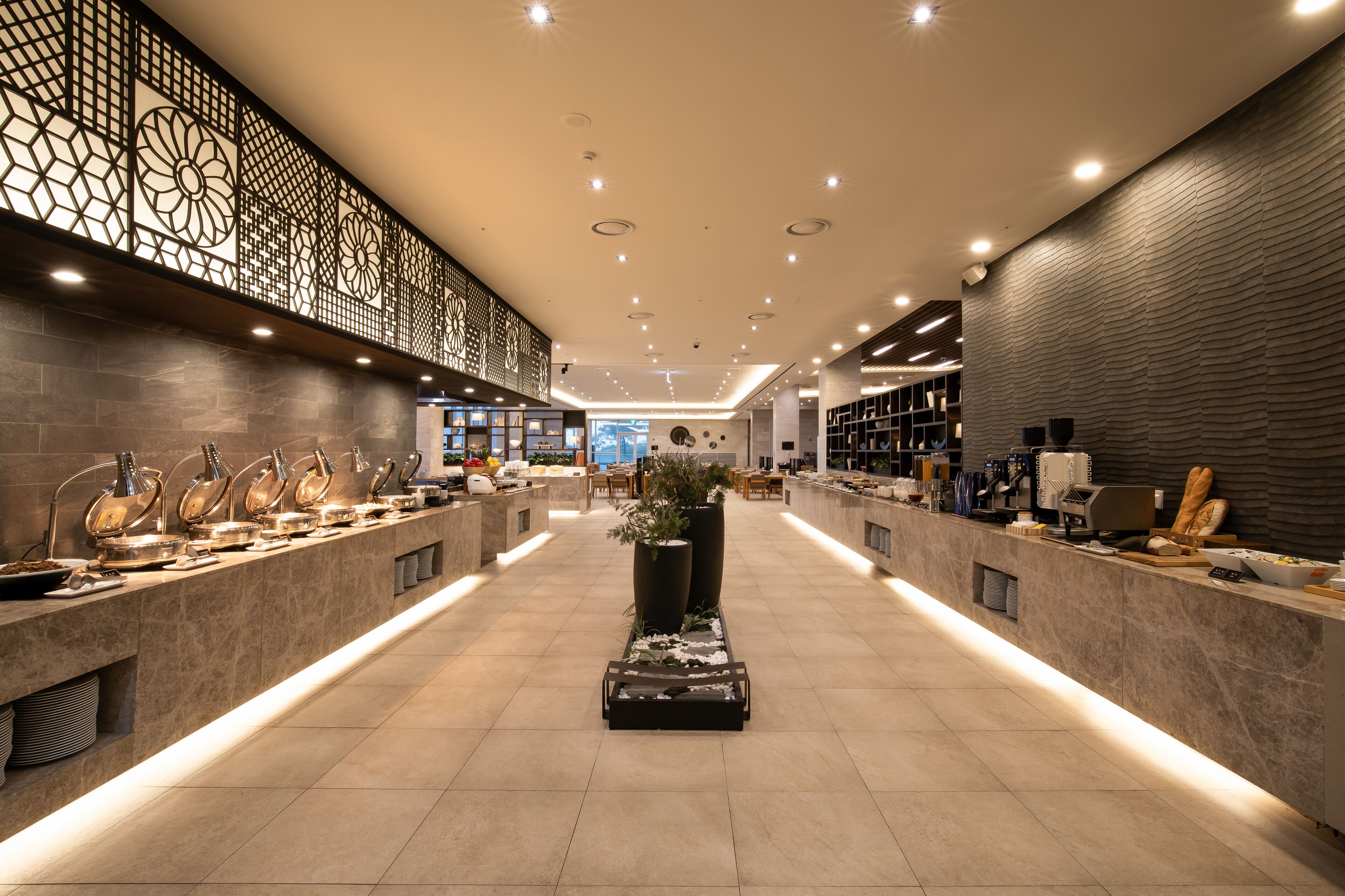 A modern hotel lobby with a long reception counter, decorative wall panels, and a central planter.