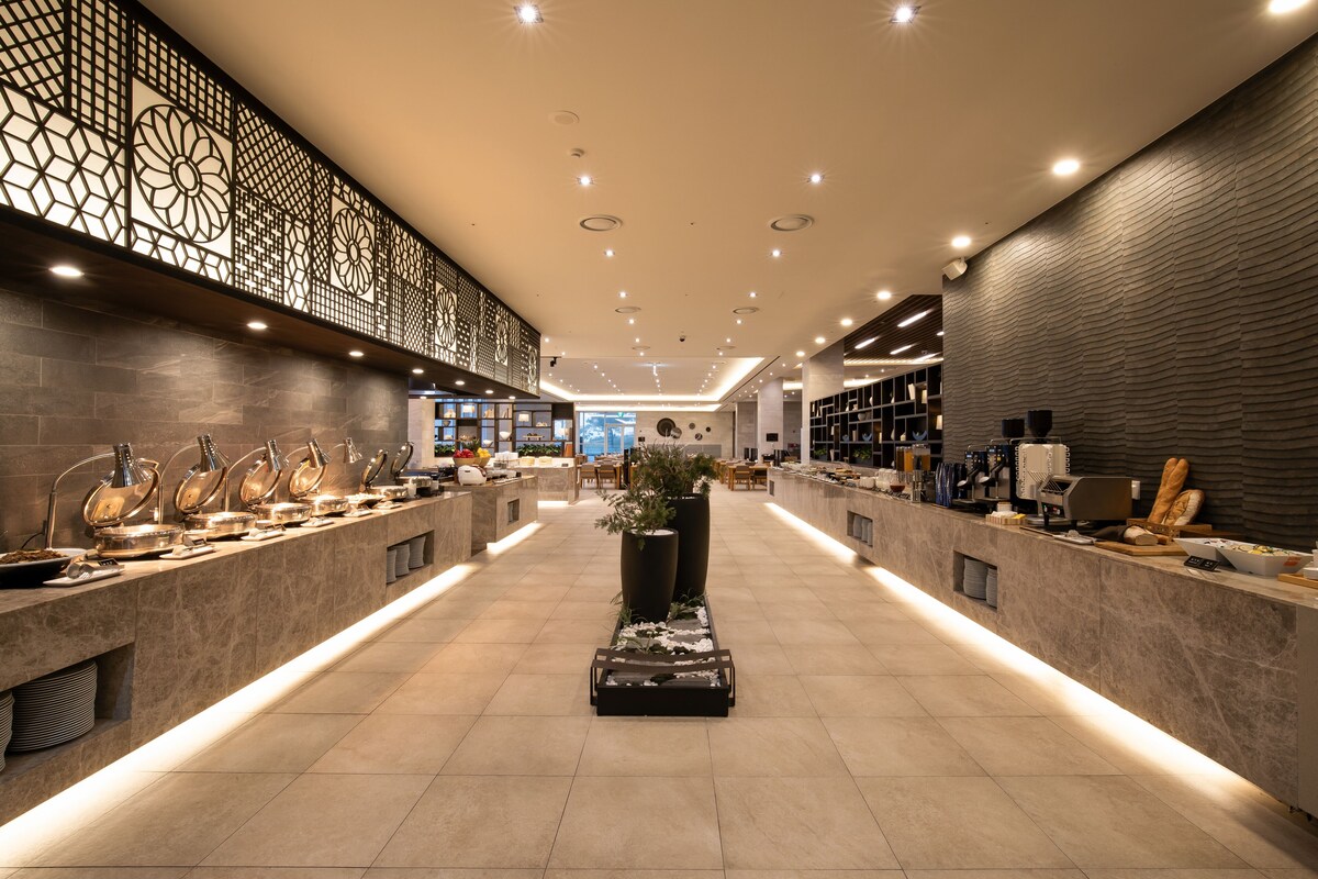 A modern hotel lobby with a long reception counter, decorative wall panels, and a central planter.