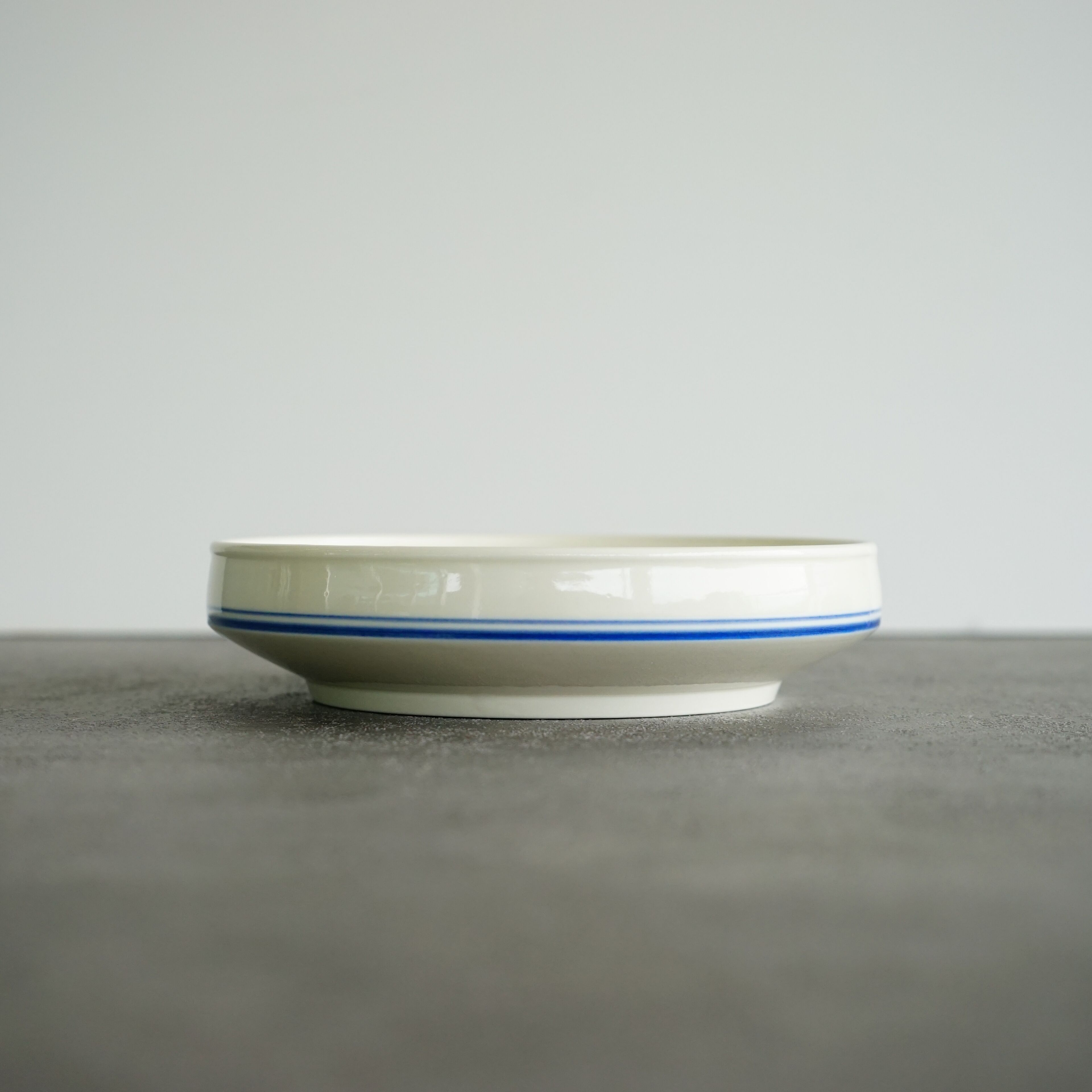A white bowl with a blue stripe on a grey surface.